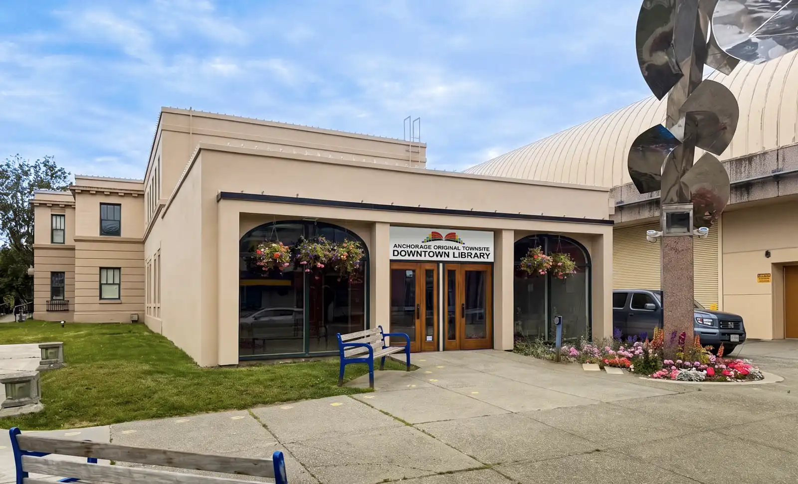 Exterior of the Downtown Library at Anchorage Original Townsite, with arched windows, benches, hanging flower baskets, and landscaped flowers