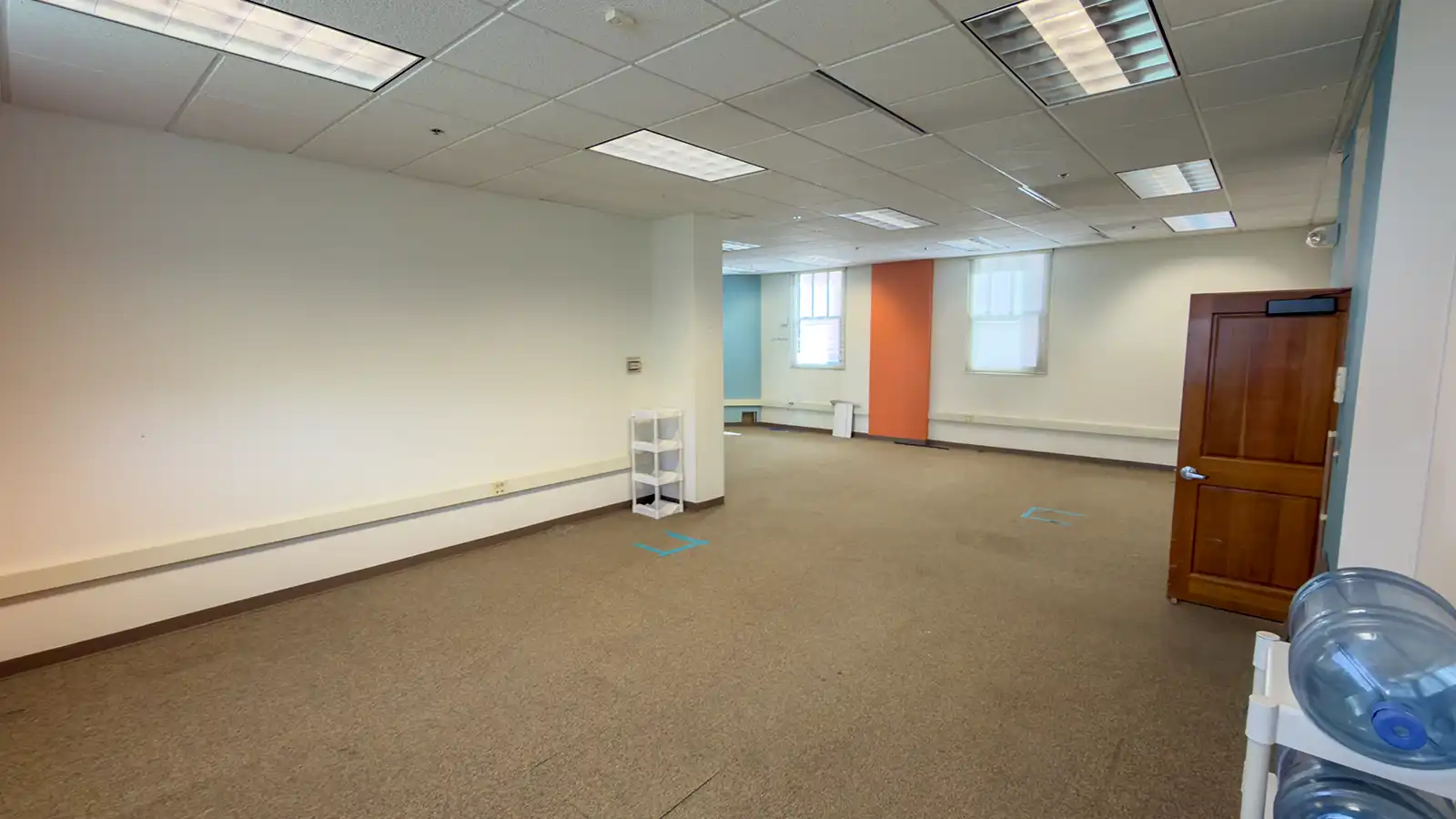 Interior room at Historic City Hall before renovation, with an open floor area, fluorescent ceiling lights, and orange and blue accent walls